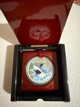 Coin with shark design in a red and black display case on a white surface